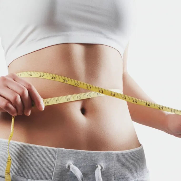 Woman measuring her waist with a tape measure, showing weight loss progress